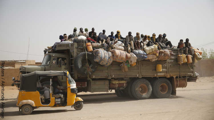 Migrants sit on their belongings in the back of a truck as it is driven through a dusty road in the desert town of Agadez, Niger