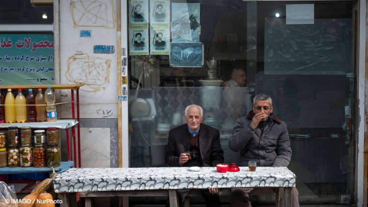 Two Iranian men sitting under portraits of Ebrahim Raisi (R) and General Qasem Soleimani, at an outdoor cafe in the Basir Thursday Bazaar (Market) in Astaneh-ye Ashrafiyeh in Gilan province March 24, 2022.