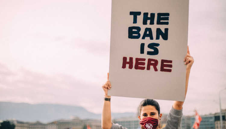 Eine Frau hält ein Schild mit The Ban is here in die Höhe.