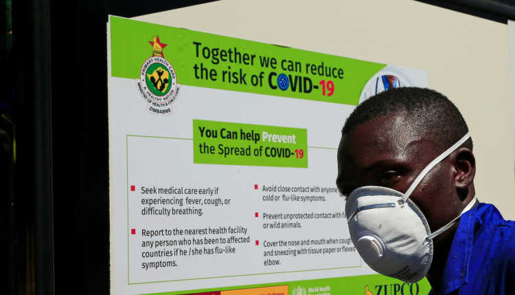 A man wearing an FSP mask stands in front of a sign with behaviours to contain the coronsvirus.