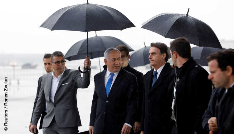 Israel's Prime Minister Netanyahu and Brazil's President Bolsonaro under umbrellas at a meeting.
