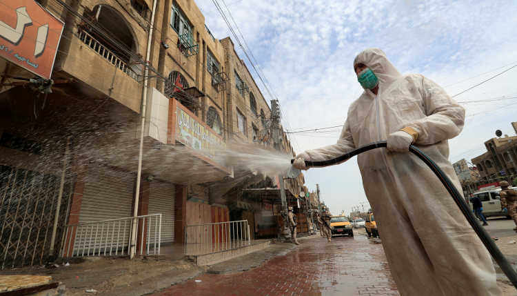 Eine Person in Schutzkleidung desinfiziert eine Straße in Bagdad.