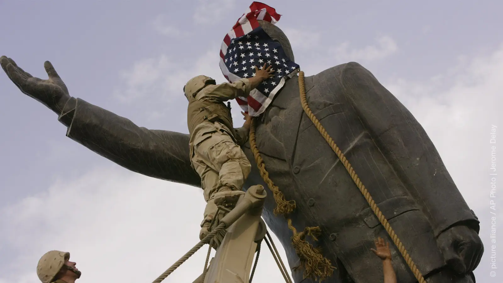  In this file photo taken Wednesday, April 9, 2003, an Iraqi man, bottom right, watches a US Marine cover the face of a statue of Saddam Hussein with an American flag before toppling the statue in downtown in Baghdad, Iraq.
