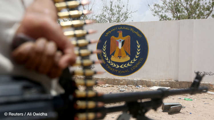 A Yemeni government soldier holds a weapon as he stands by an emblem of the STC at the headquarters of the separatist Southern Transitional Council in Ataq, Yemen.
