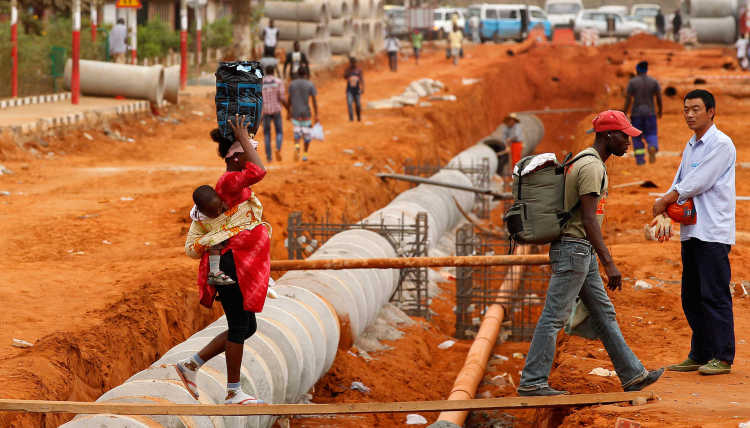 A Chinese construction worker looks on as locals cross a construction site using a makeshift bridge in Viana, about 30 km east of the capital Luanda.