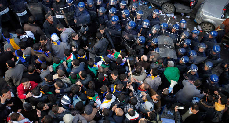 Demonstrators in Algeria stand in front of a police barricade.