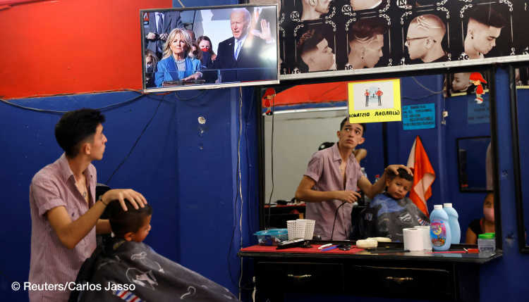 A Colombian migrant at a hair salon in Tapachula, Mexico, watches the swearing in of Joe Biden as president of the United States while at work.