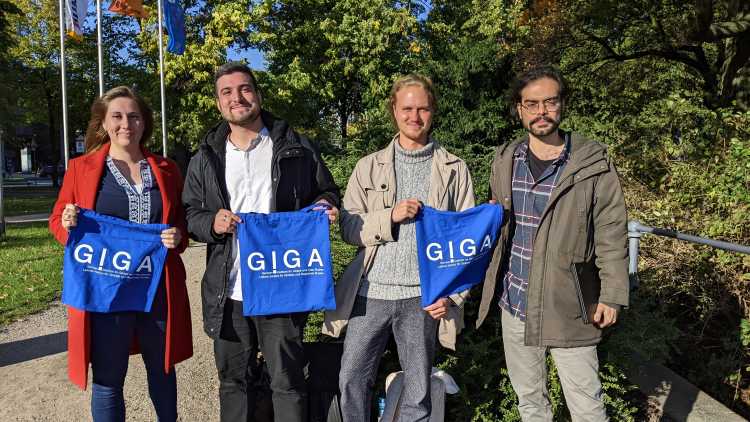 Neue Doktoranden stehen an der Alster in Hamburg und halten GIGA-Taschen in der Hand.