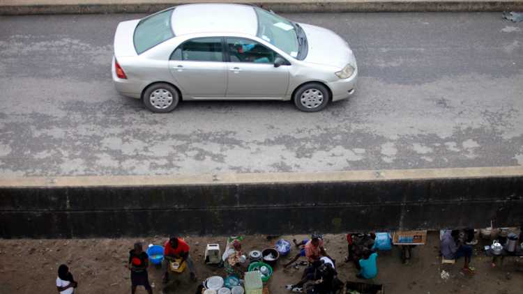 Afrikaner sitzen am Straßenrand während ein neues Auto vorbeifährt