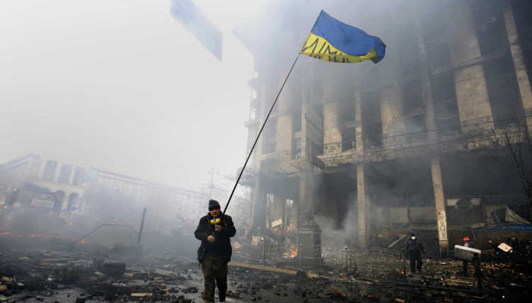 An anti-government protester holds a Ukranian flag as he advances through burning barricades in Kiev's Independence Square. 