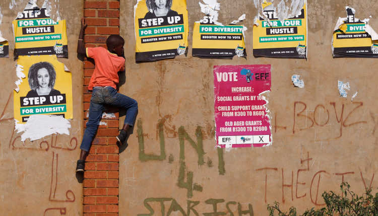 A boy climbs up a wall with election posters in South Africa.