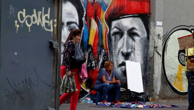 People in front of a Chavez graffiti in Venezuela