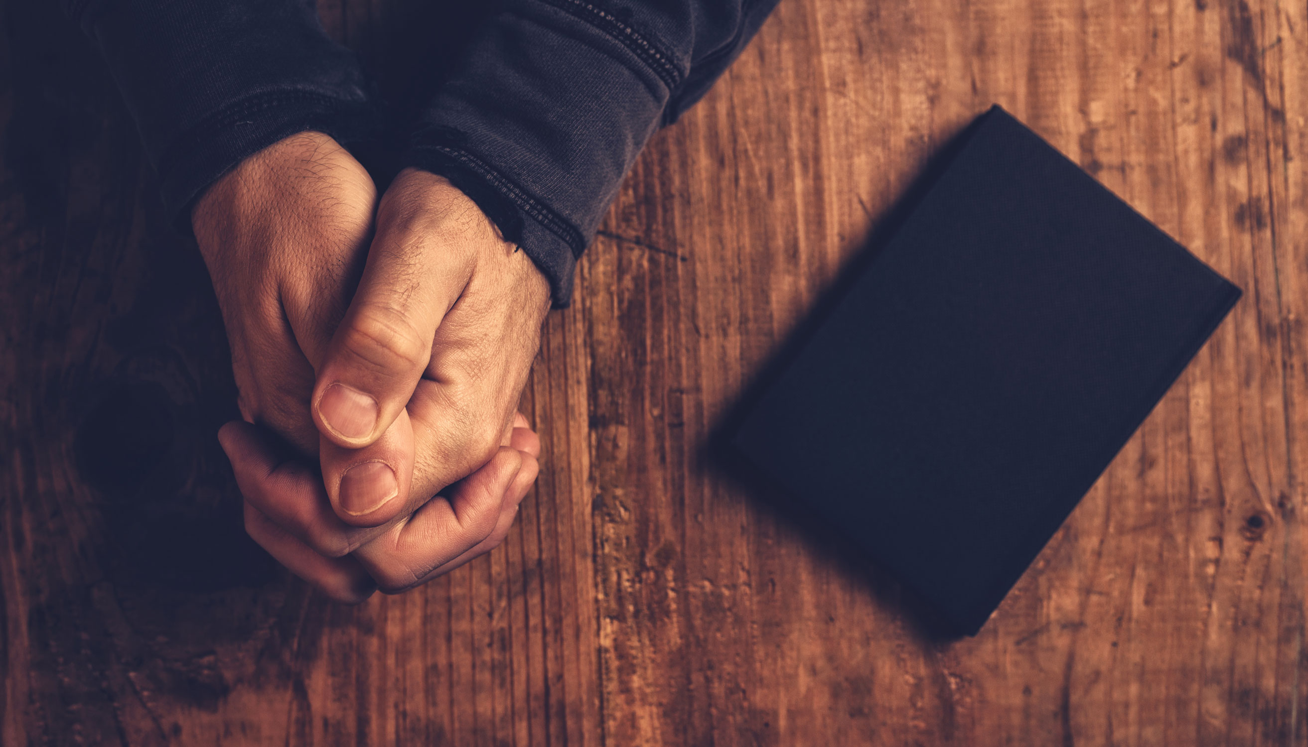 Interlaced hands on a table next to a prayer book.